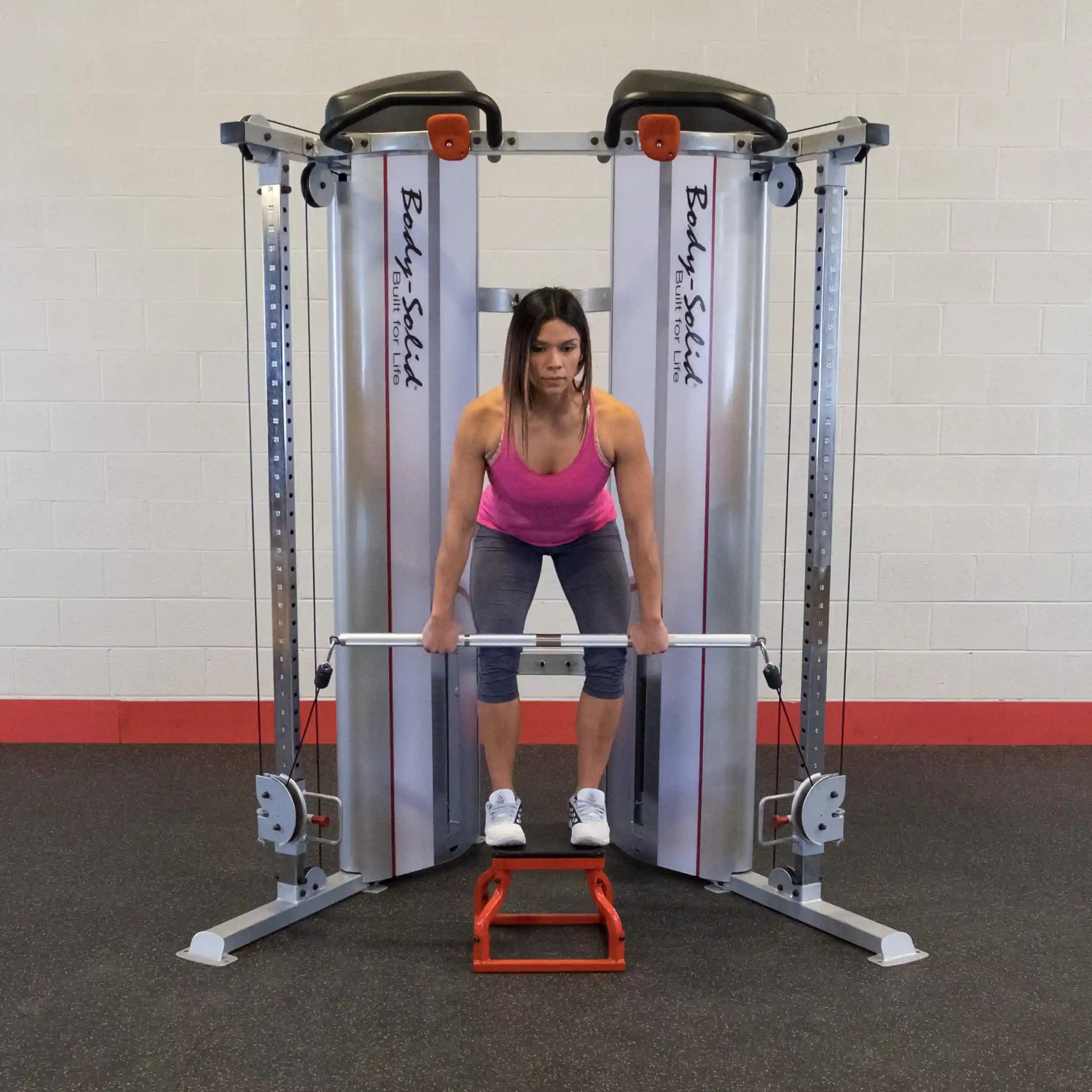 A woman performing a deadlift using the Body-Solid Pro ClubLine Series 2 Functional Trainer S2FT, standing on a red platform with a barbell in her hands.