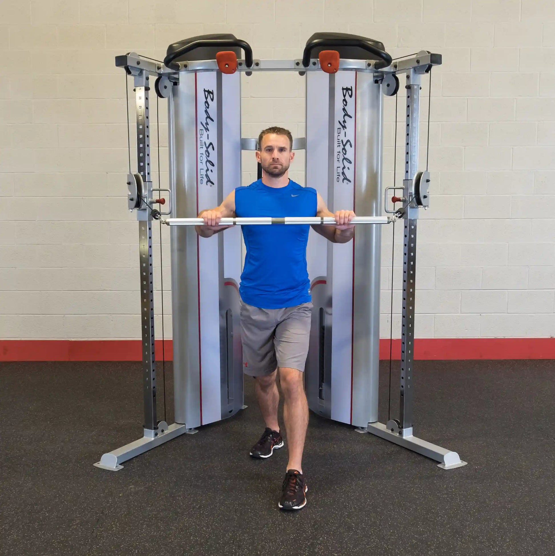 A man performing an exercise with a barbell in front of the Body-Solid Pro ClubLine Series 2 Functional Trainer S2FT in a gym setting.