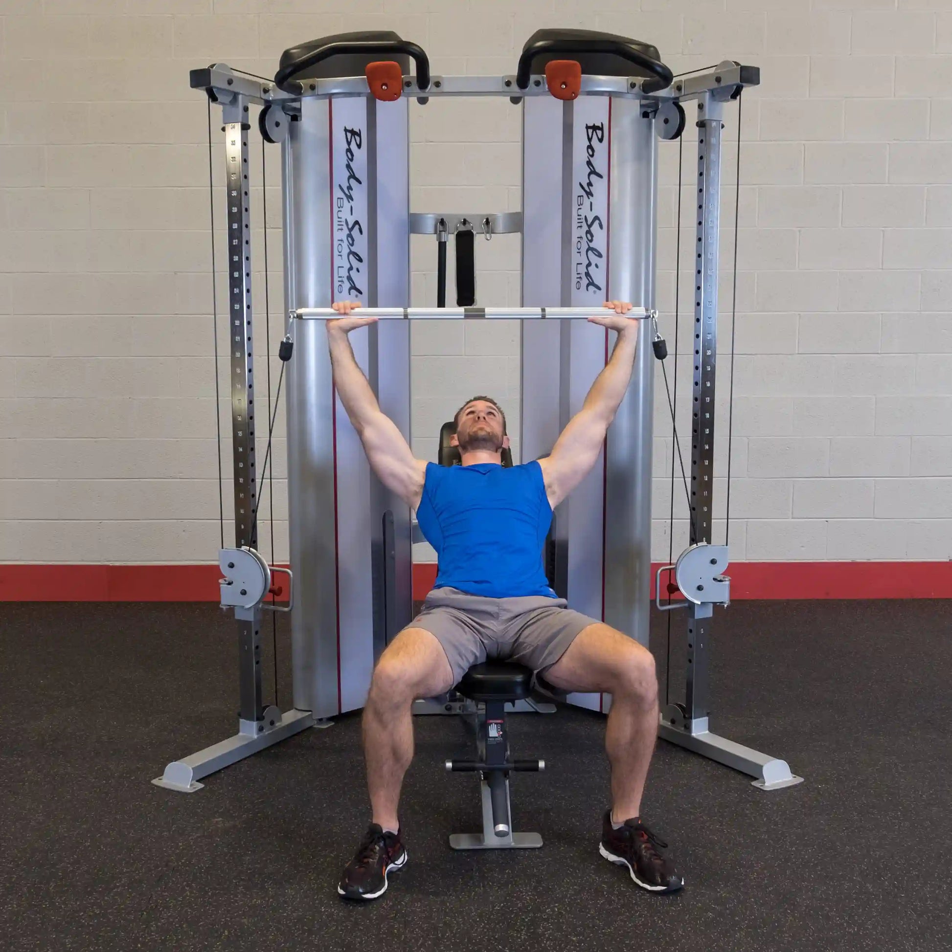 A man in a blue tank top performs an overhead press using the Body-Solid Pro ClubLine Series 2 Functional Trainer S2FT in a gym setting.