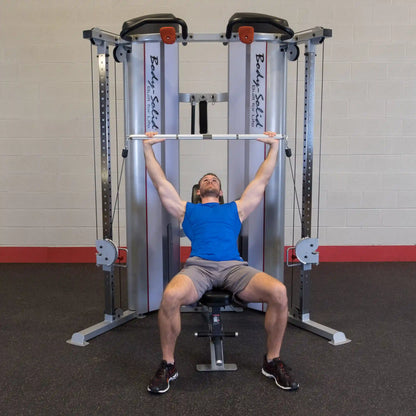 A man in a blue tank top performs an overhead press using the Body-Solid Pro ClubLine Series 2 Functional Trainer S2FT in a gym setting.