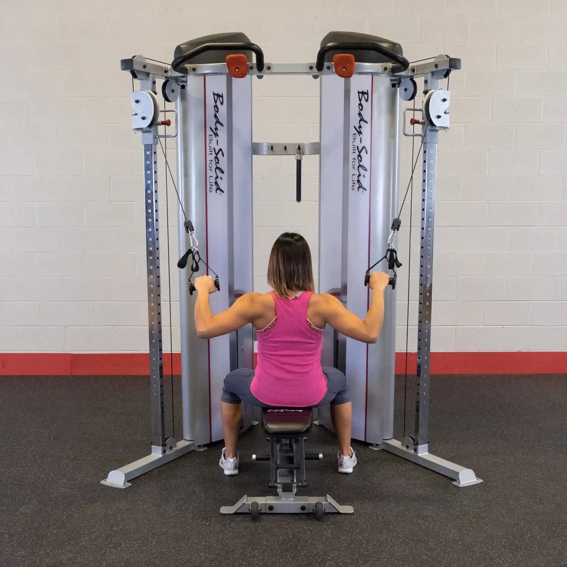 A person using the Body-Solid Pro ClubLine Series 2 Functional Trainer S2FT, seated on a bench and pulling cables with both hands, in a gym setting.