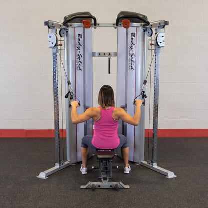 A person using the Body-Solid Pro ClubLine Series 2 Functional Trainer S2FT, seated on a bench and pulling cables with both hands, in a gym setting.