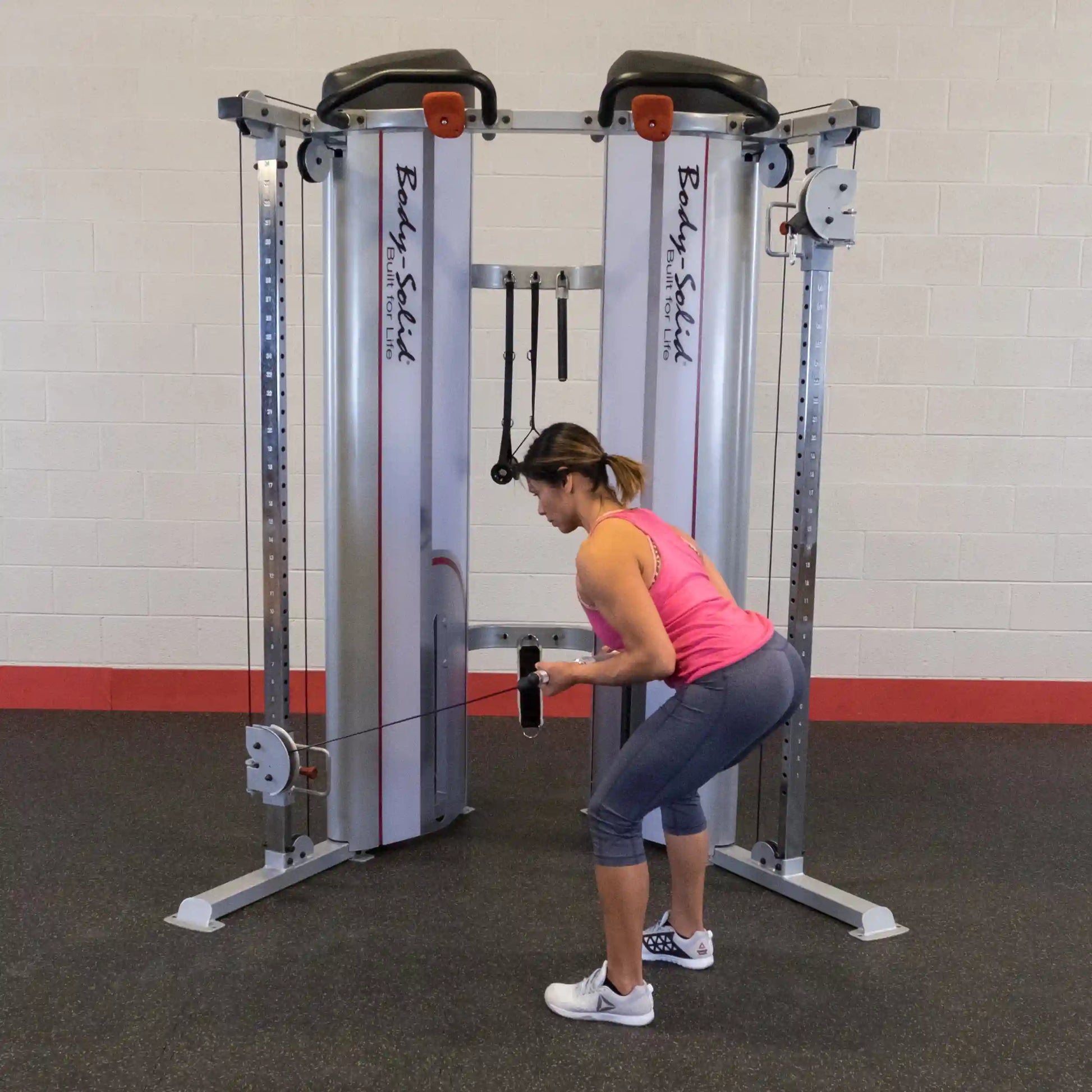 A woman performs an exercise using the Body-Solid Pro ClubLine Series 2 Functional Trainer S2FT, demonstrating a bent-over position while holding the cable attachment.