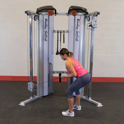 A woman performs an exercise using the Body-Solid Pro ClubLine Series 2 Functional Trainer S2FT, demonstrating a bent-over position while holding the cable attachment.