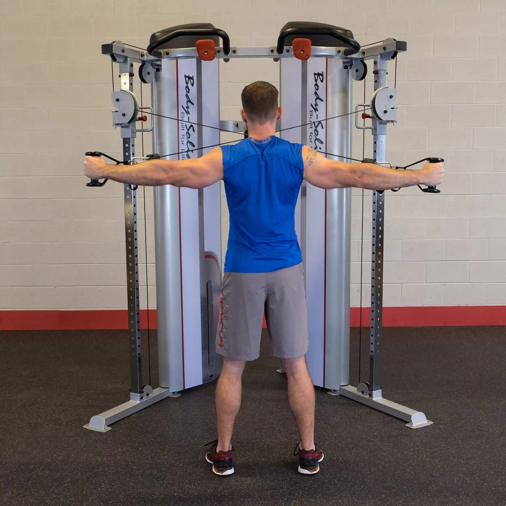 A man performing an exercise with the Body-Solid Pro ClubLine Series 2 Functional Trainer S2FT, standing with arms extended to the sides.
