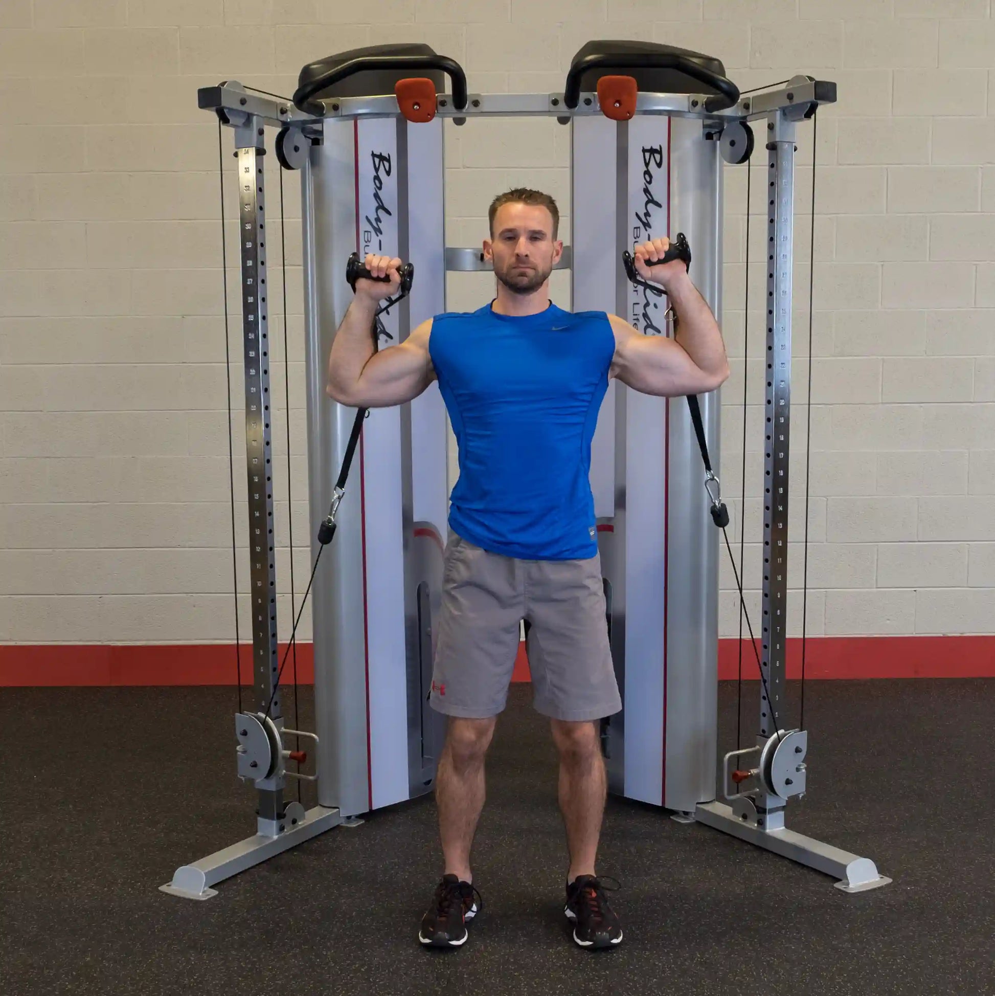 A person demonstrating an exercise using the Body-Solid Pro ClubLine Series 2 Functional Trainer S2FT, standing with arms raised and holding cables.