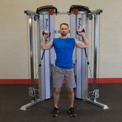 A person demonstrating an exercise using the Body-Solid Pro ClubLine Series 2 Functional Trainer S2FT, standing with arms raised and holding cables.