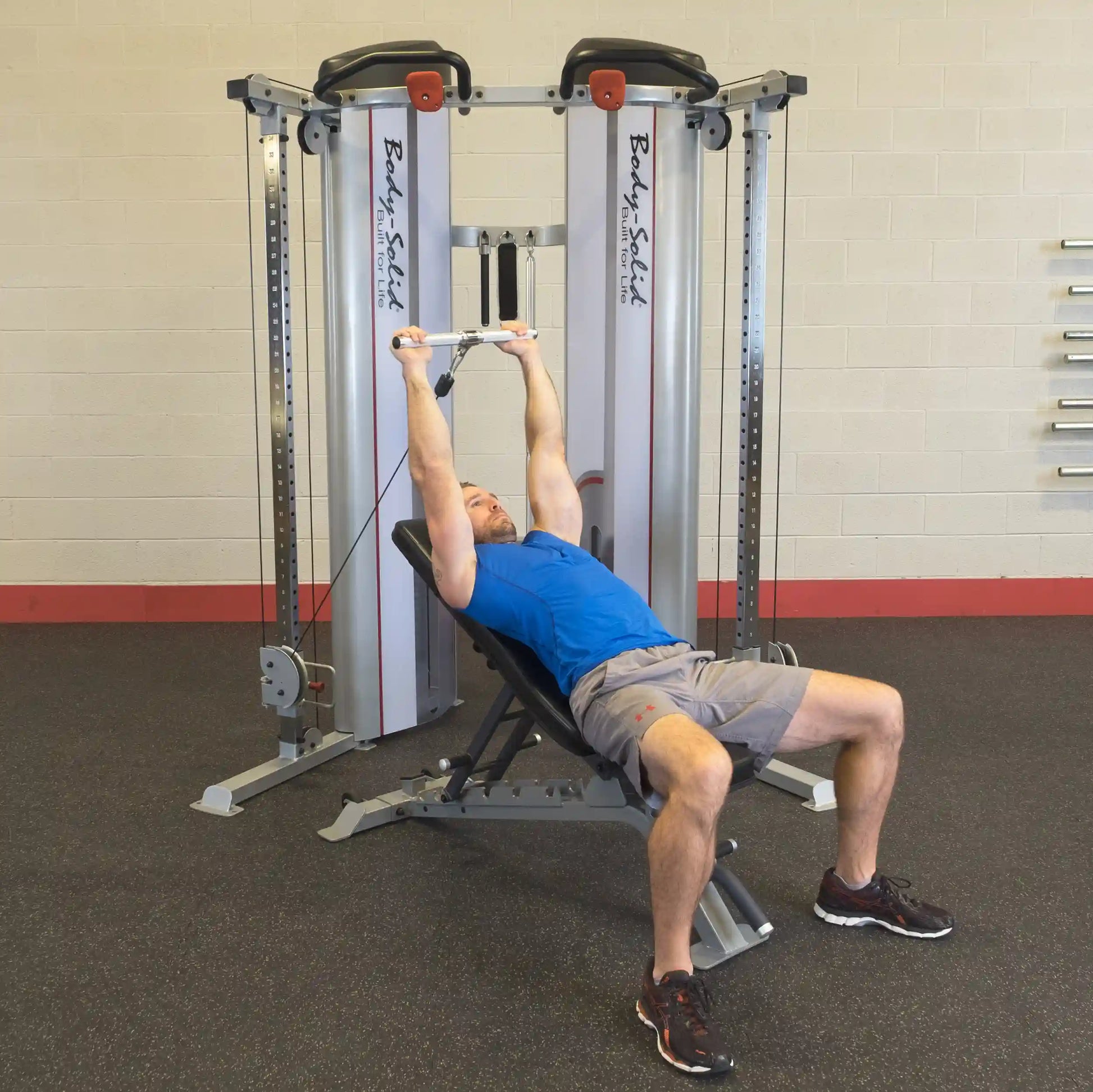 A person performing an exercise on the Body-Solid Pro ClubLine Series 2 Functional Trainer S2FT, lying on a bench with arms extended above holding onto the cable attachment.