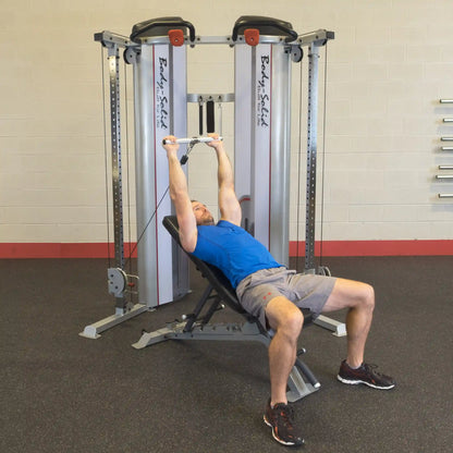 A person performing an exercise on the Body-Solid Pro ClubLine Series 2 Functional Trainer S2FT, lying on a bench with arms extended above holding onto the cable attachment.