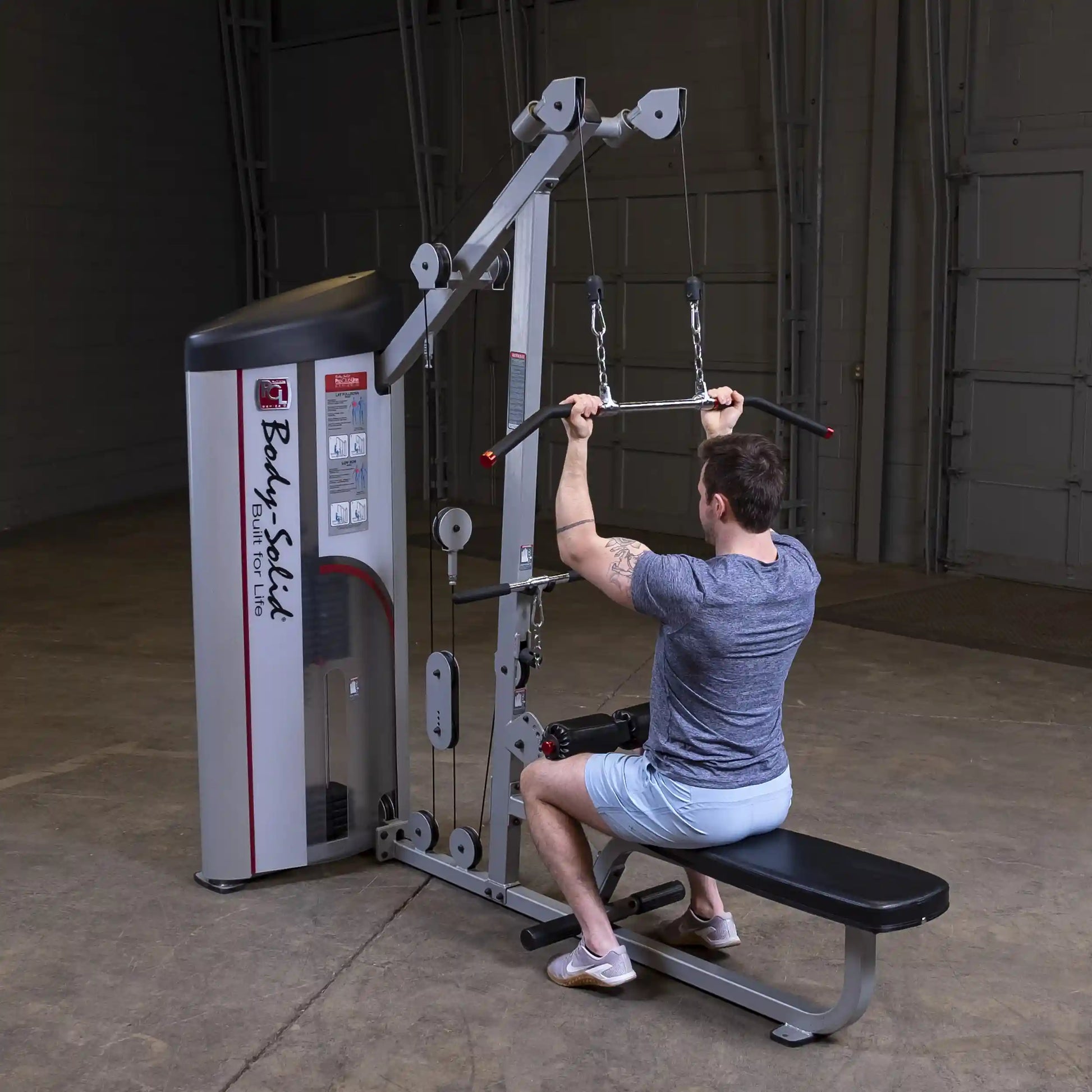 A person using the Body-Solid Pro ClubLine Series 2 Lat Pulldown & Seated Row Machine S2LAT, performing a lat pulldown exercise in a gym setting.