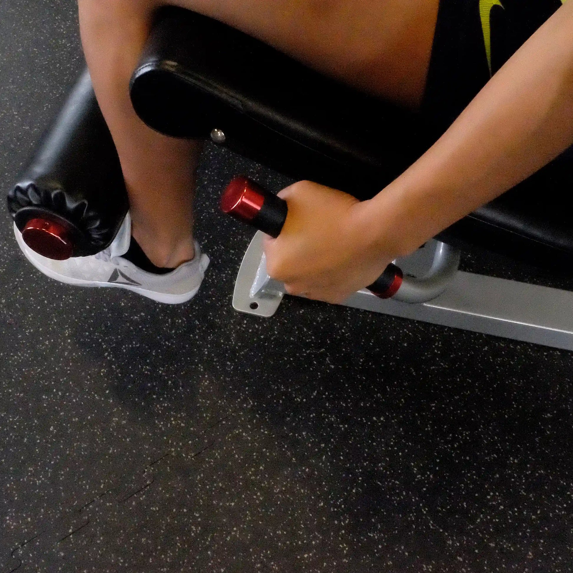 Close-up of a person's hand gripping the handle of the Body-Solid Pro ClubLine Series 2 Leg Extension & Leg Curl Machine S2LEC, with a focus on the leg support and foot positioning.