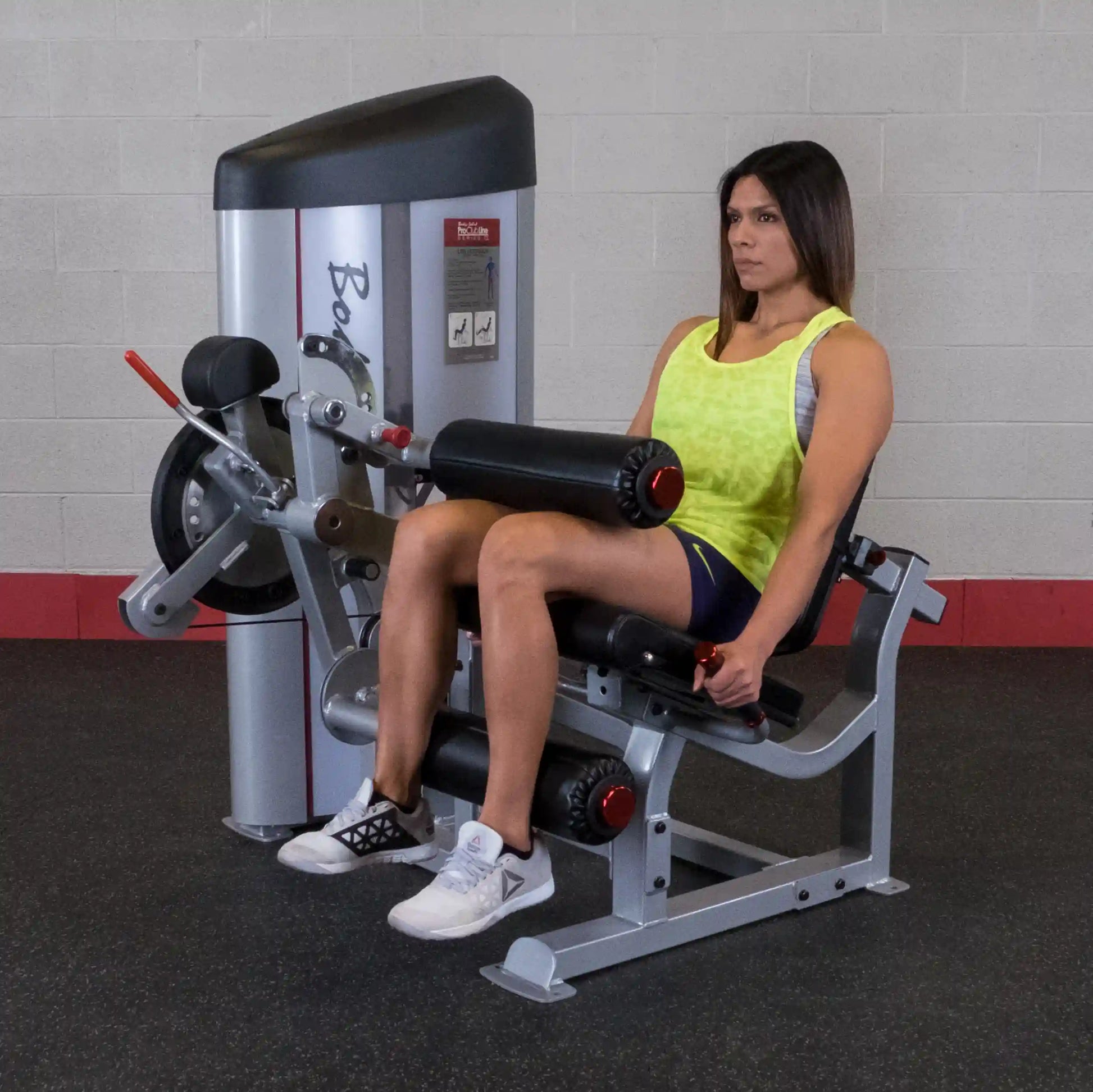 A woman using the Body-Solid Pro ClubLine Series 2 Leg Extension & Leg Curl Machine S2LEC in a gym setting, demonstrating leg extension exercise.