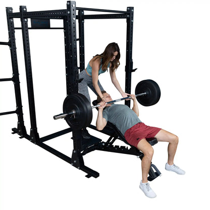 A man performs a bench press with the Body-Solid Pro ClubLine Spotter Platforms SPRSP, assisted by a woman, in a gym setting.