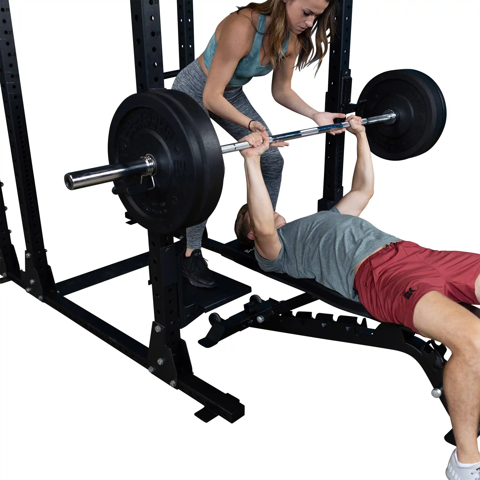 A man performing a bench press with support from a woman using Body-Solid Pro ClubLine Spotter Platforms SPRSP, showcasing strength training in a gym setting.