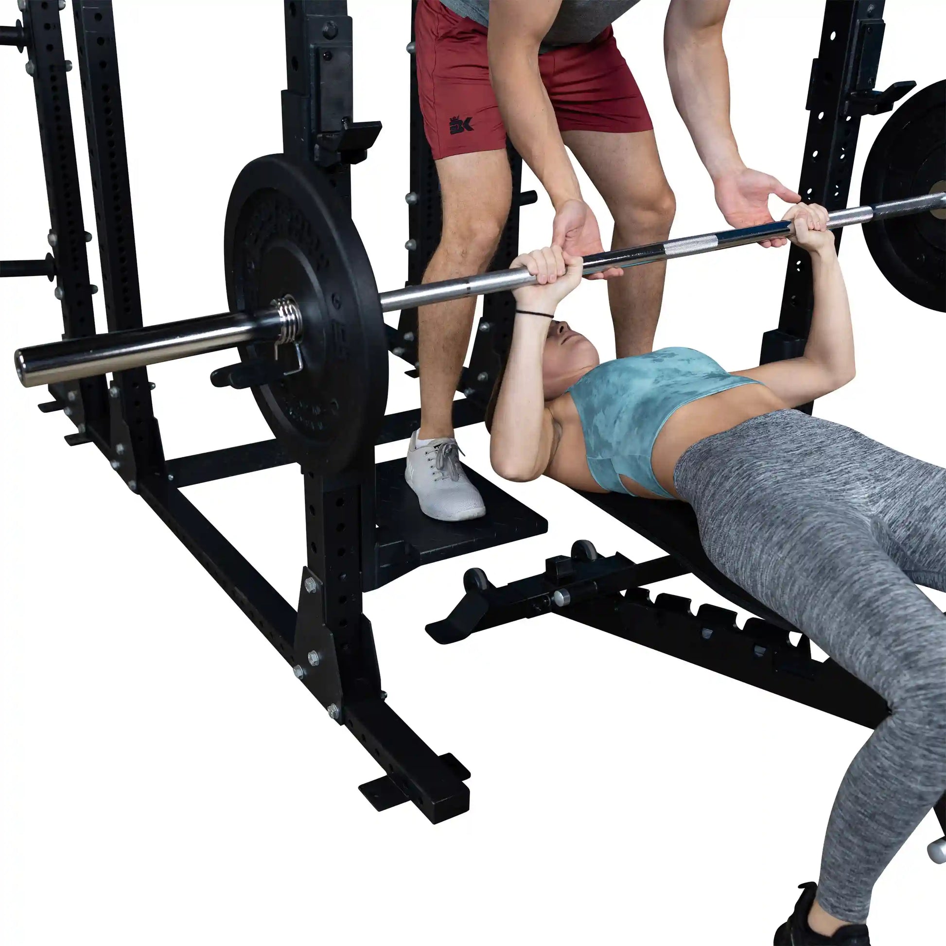 A woman performing a bench press with assistance from a male spotter, using the Body-Solid Pro ClubLine Spotter Platforms SPRSP for safety and support.
