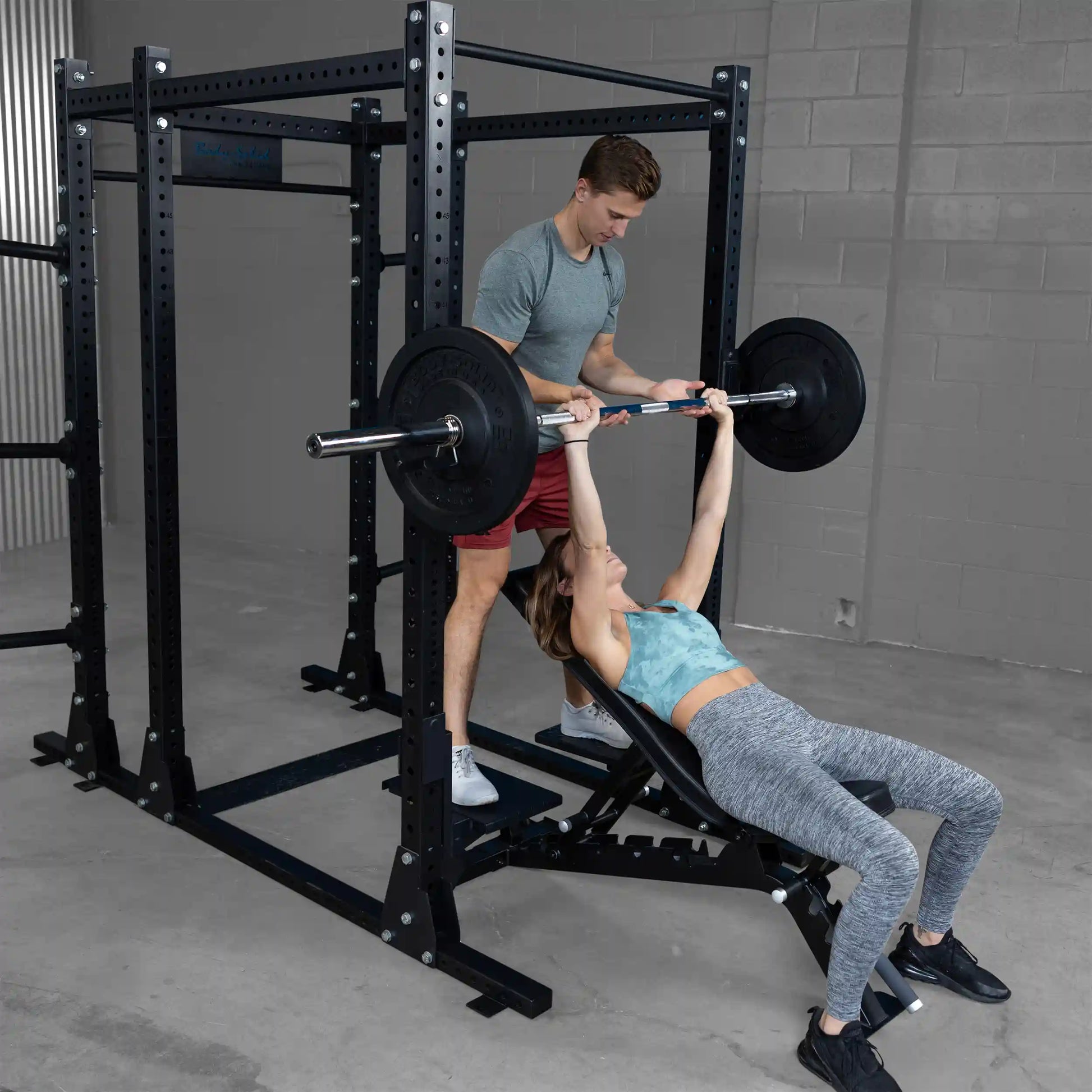 Two individuals using the Body-Solid Pro ClubLine Spotter Platforms SPRSP for a bench press exercise, with one spotting the other inside a gym setting.