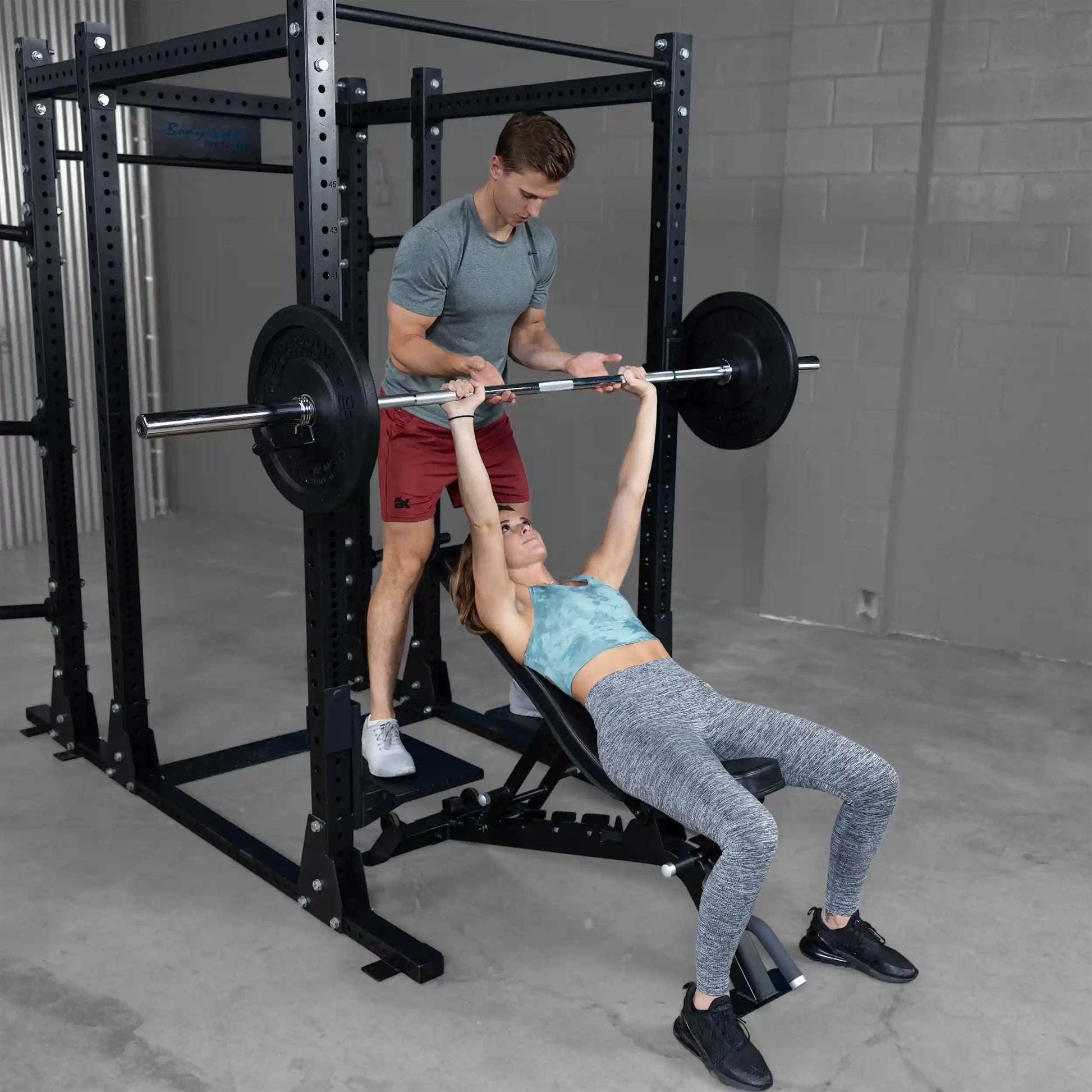 A male trainer assisting a female lifter using the Body-Solid Pro ClubLine Spotter Platforms SPRSP while she performs a bench press exercise.