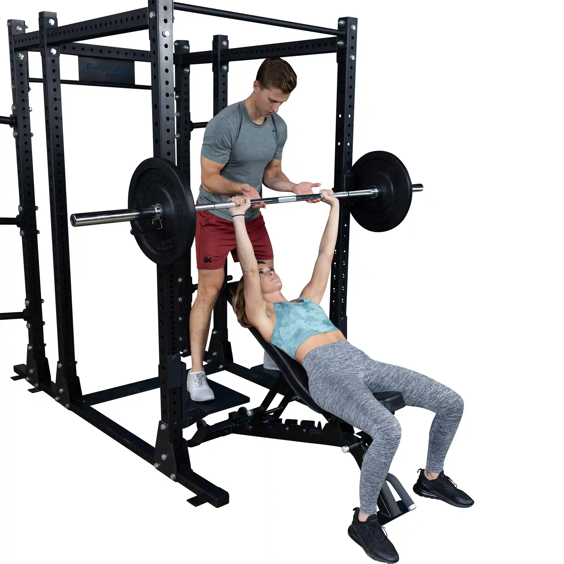 A man assists a woman during a bench press using the Body-Solid Pro ClubLine Spotter Platforms SPRSP, showcasing proper lifting technique and support.