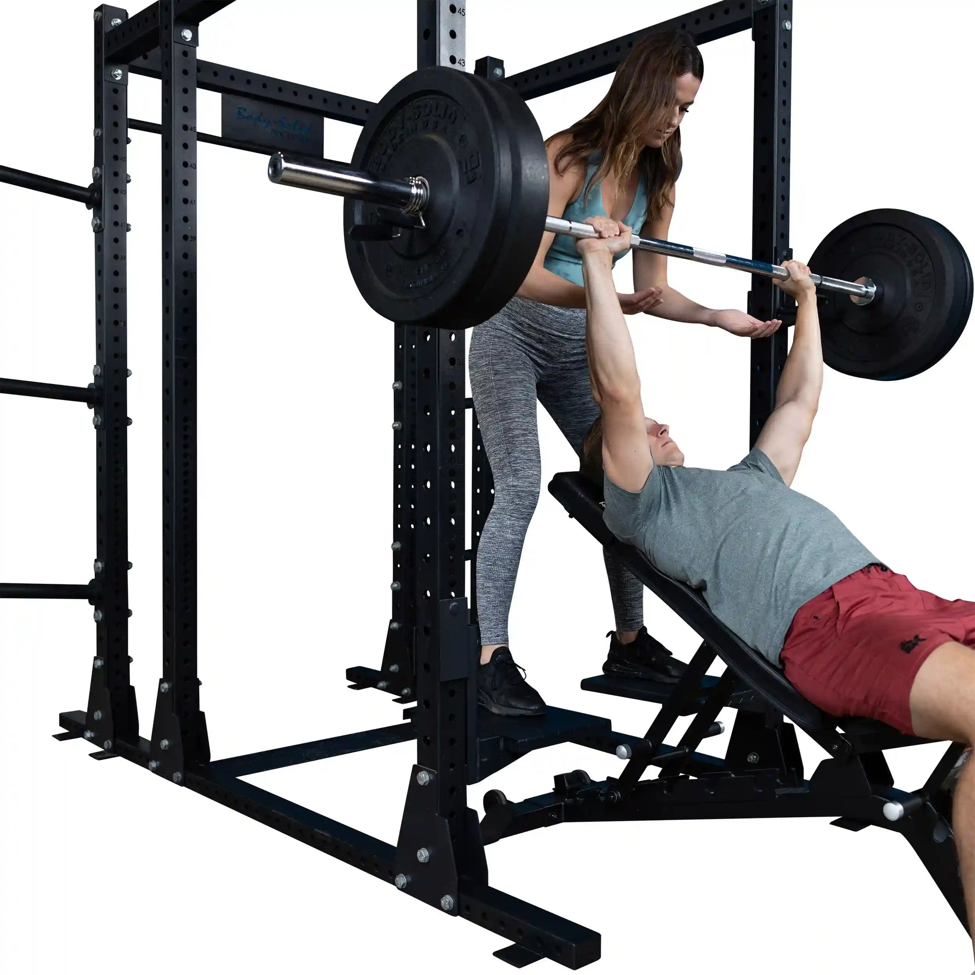 A man bench pressing weights with the assistance of a woman in a gym, using the Body-Solid Pro ClubLine Spotter Platforms SPRSP for safety and support.