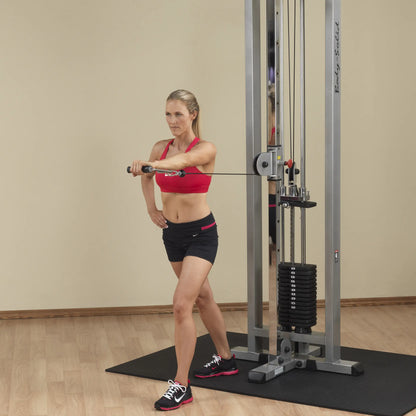 A woman performing an exercise on the Body-Solid Pro Clubline Cable Crossover SCC1200G, demonstrating proper form while using the cable machine in a gym setting.