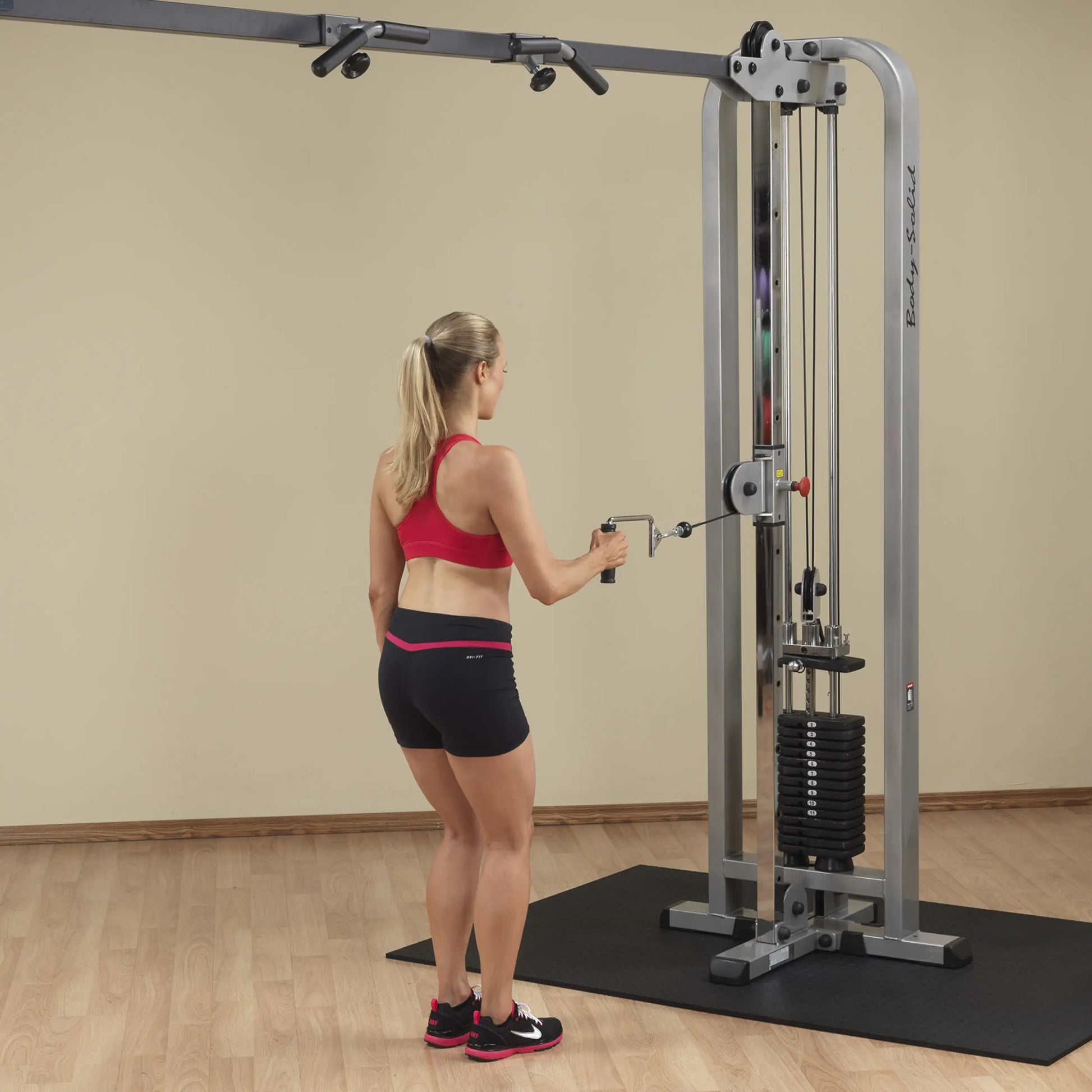 A woman in athletic wear using the Body-Solid Pro Clubline Cable Crossover SCC1200G in a gym setting.