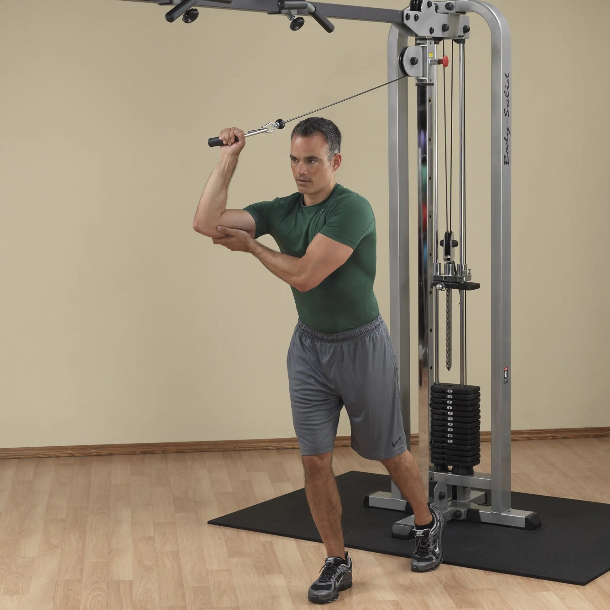 A man demonstrating an exercise using the Body-Solid Pro Clubline Cable Crossover SCC1200G, performing a cable crossover movement in a fitness studio.