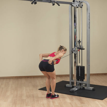A woman performs an exercise using the Body-Solid Pro Clubline Cable Crossover SCC1200G, focusing on her back muscles, in a gym setting with a wooden floor and neutral wall.