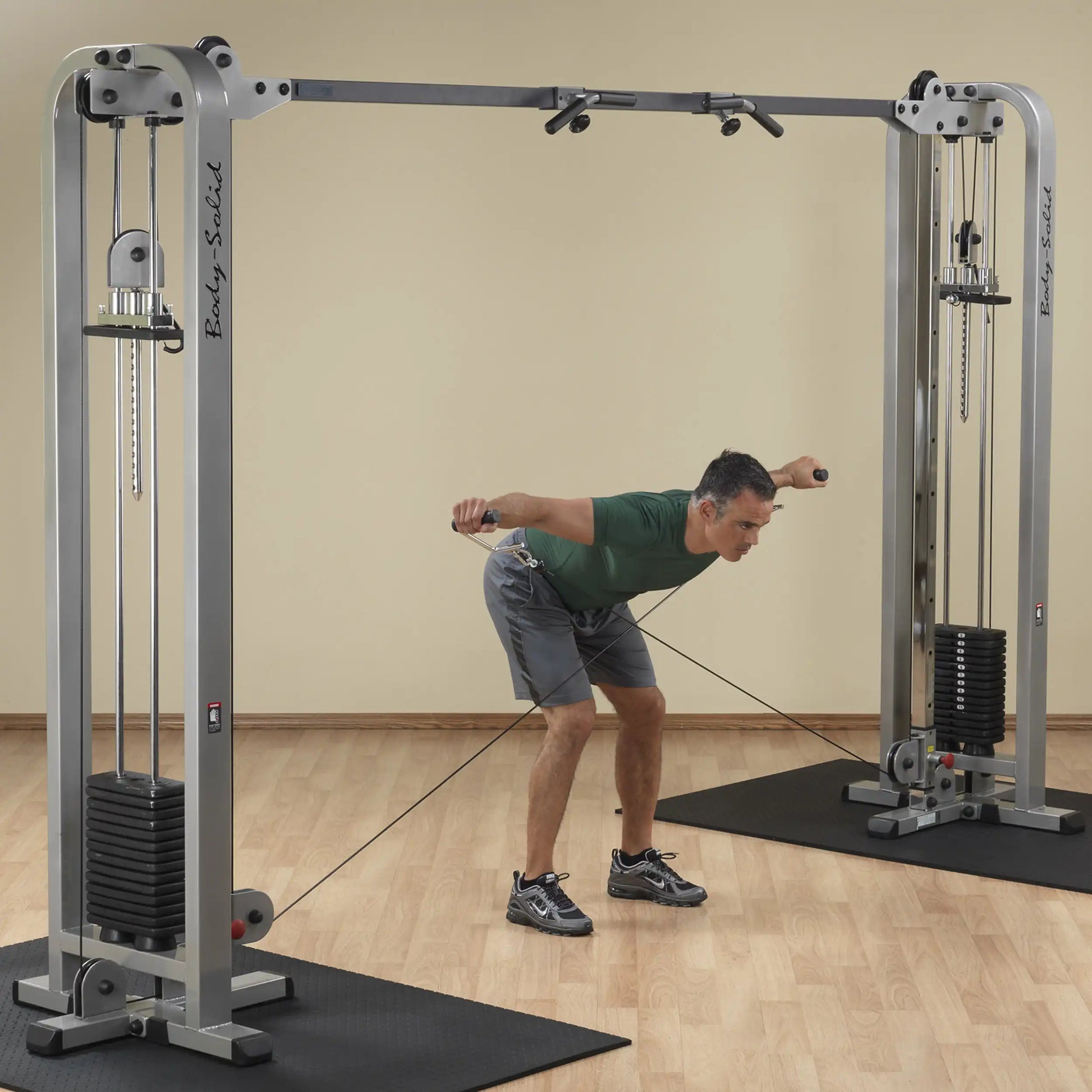 A man performing an exercise using the Body-Solid Pro Clubline Cable Crossover SCC1200G in a gym setting, demonstrating proper form while pulling cables from both sides.