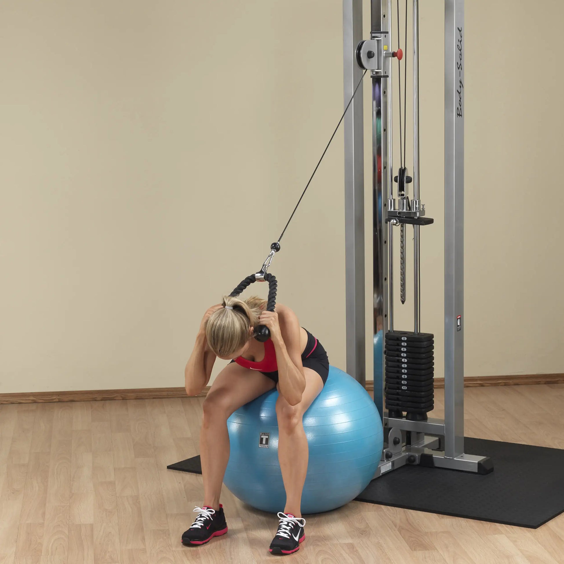 A person performing an exercise on a blue stability ball while using the Body-Solid Pro Clubline Cable Crossover SCC1200G, focusing on cable resistance training.
