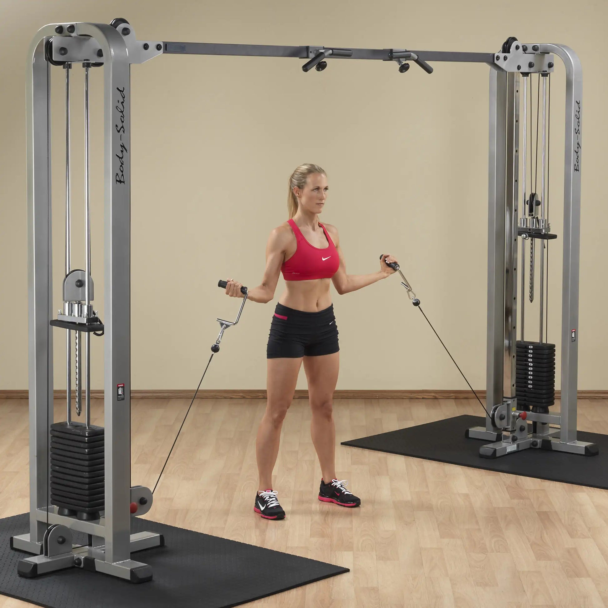 A woman performing an exercise with the Body-Solid Pro Clubline Cable Crossover SCC1200G, using cables from both sides while standing on a gym floor.