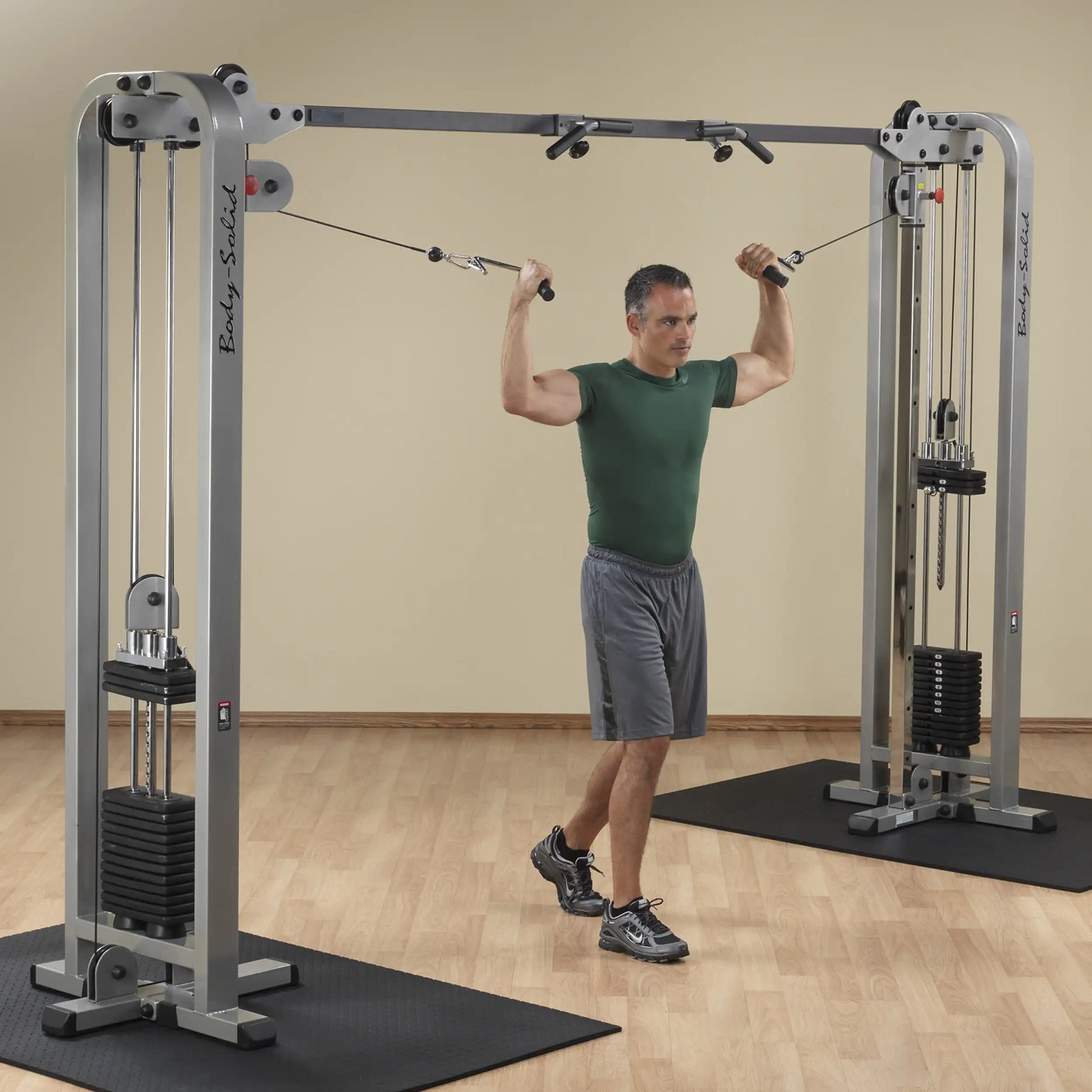 A man performing an exercise using the Body-Solid Pro Clubline Cable Crossover SCC1200G, with cables attached to a dual pulley system, in a gym setting.