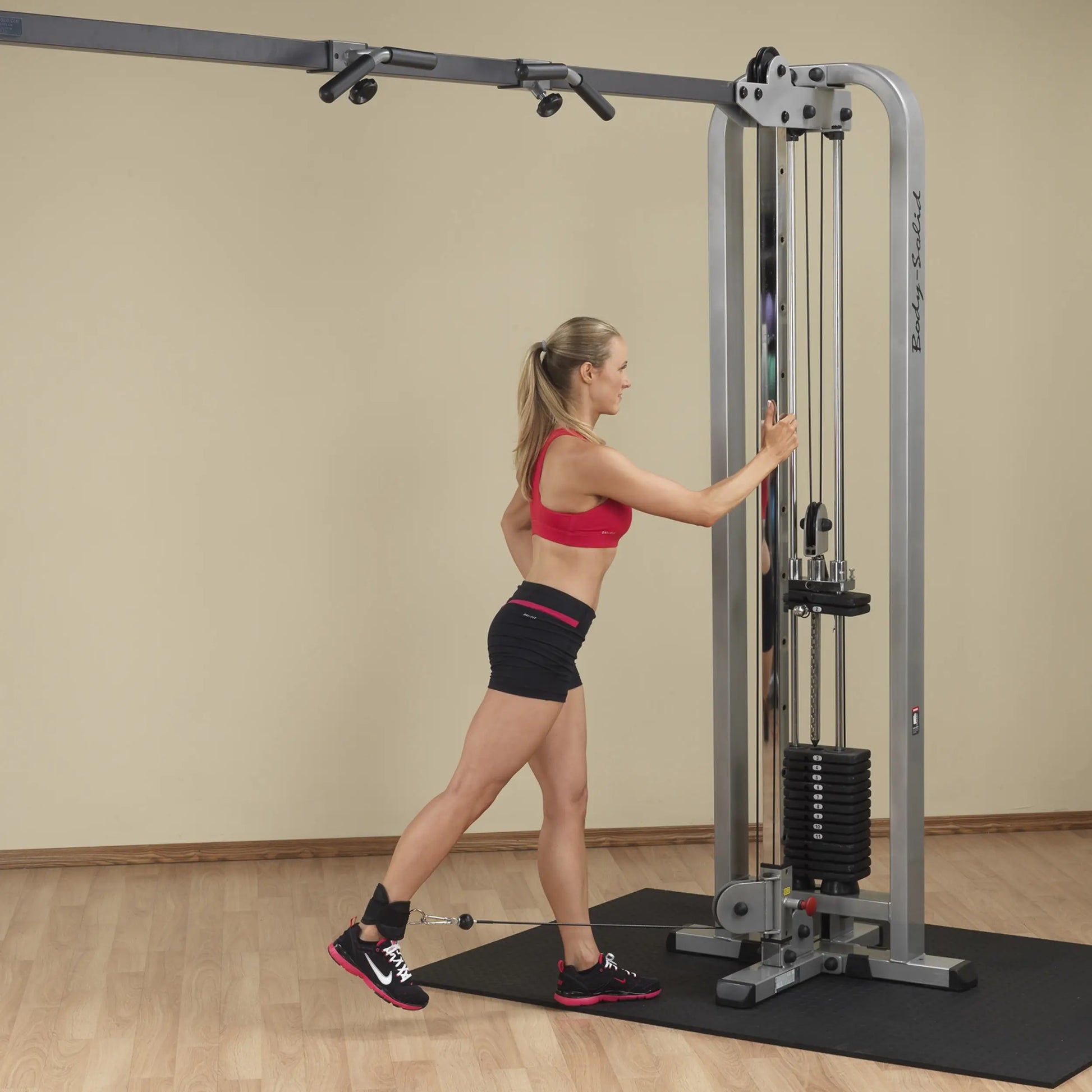 A woman performs an exercise using the Body-Solid Pro Clubline Cable Crossover SCC1200G, demonstrating strength training techniques in a gym setting.
