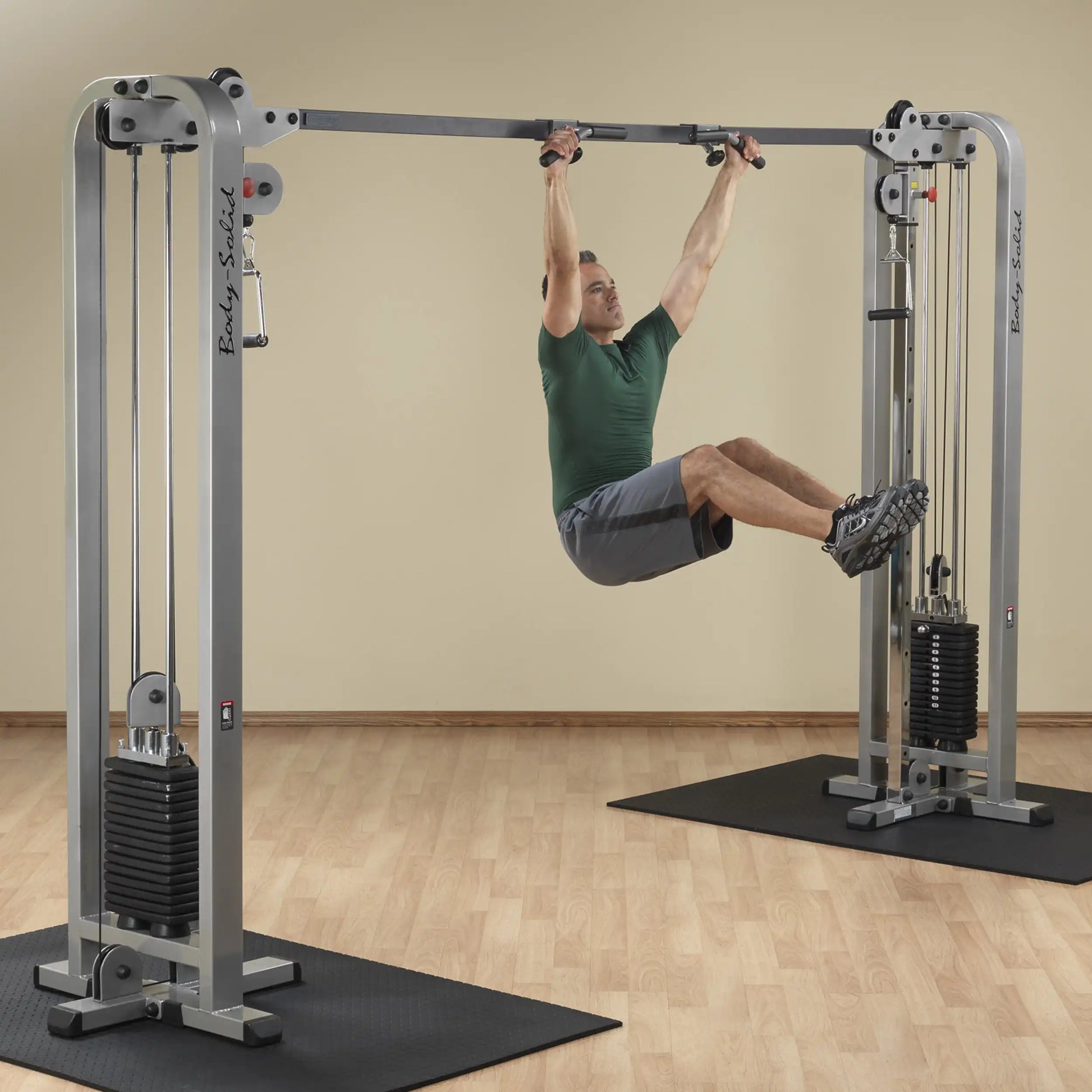 A man using the Body-Solid Pro Clubline Cable Crossover SCC1200G for a workout, performing an exercise while suspended between two cable machines in a gym setting.