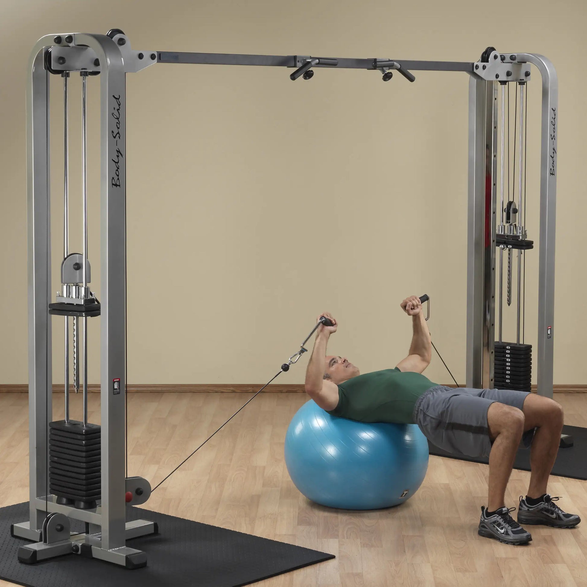 A person performing an exercise on a stability ball using the Body-Solid Pro Clubline Cable Crossover SCC1200G, featuring dual cable pulleys and adjustable handles in a fitness studio setting.
