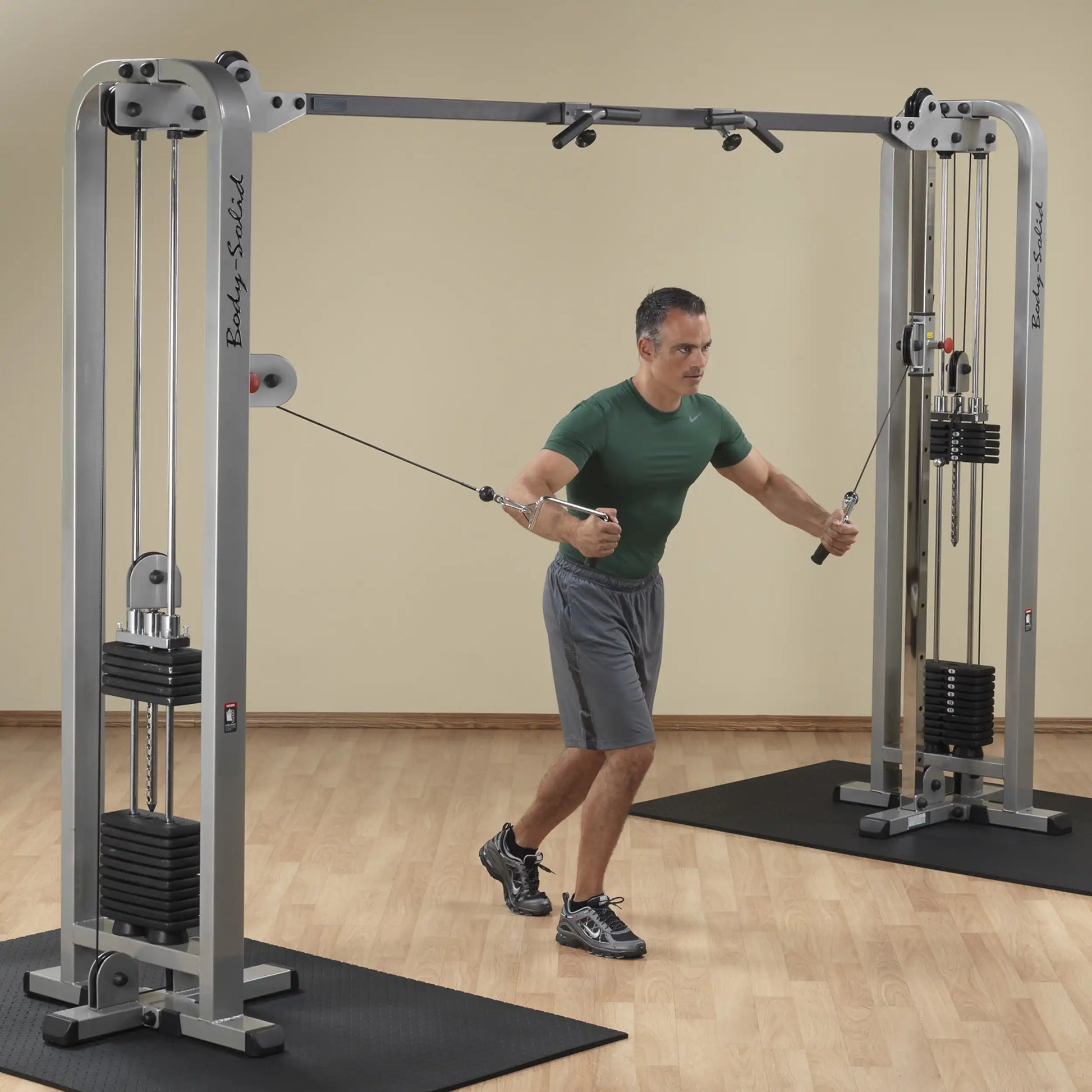 A man performing an exercise using the Body-Solid Pro Clubline Cable Crossover SCC1200G in a fitness studio, showcasing the cable machine and weights.