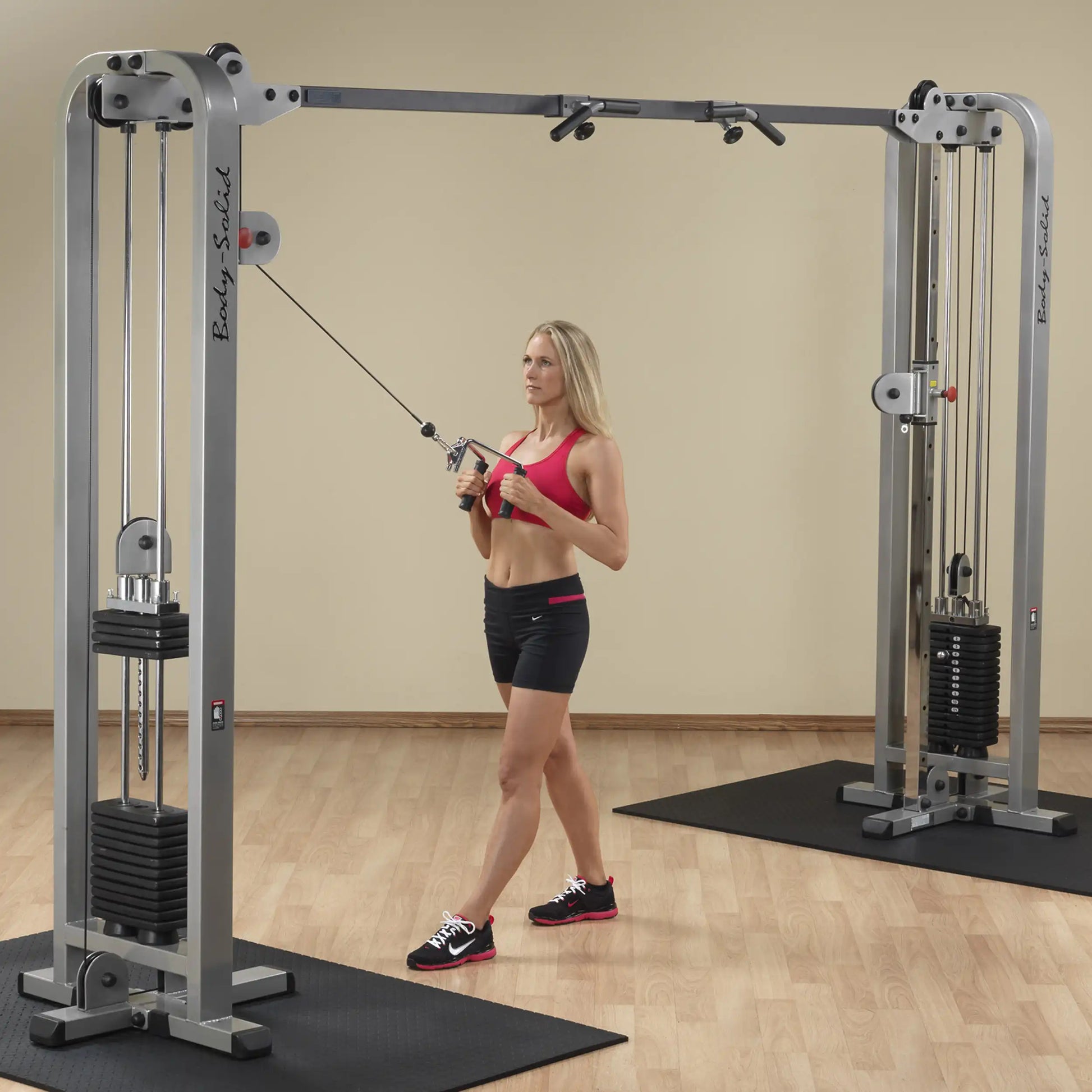 A woman performing an exercise using the Body-Solid Pro Clubline Cable Crossover SCC1200G in a gym setting.