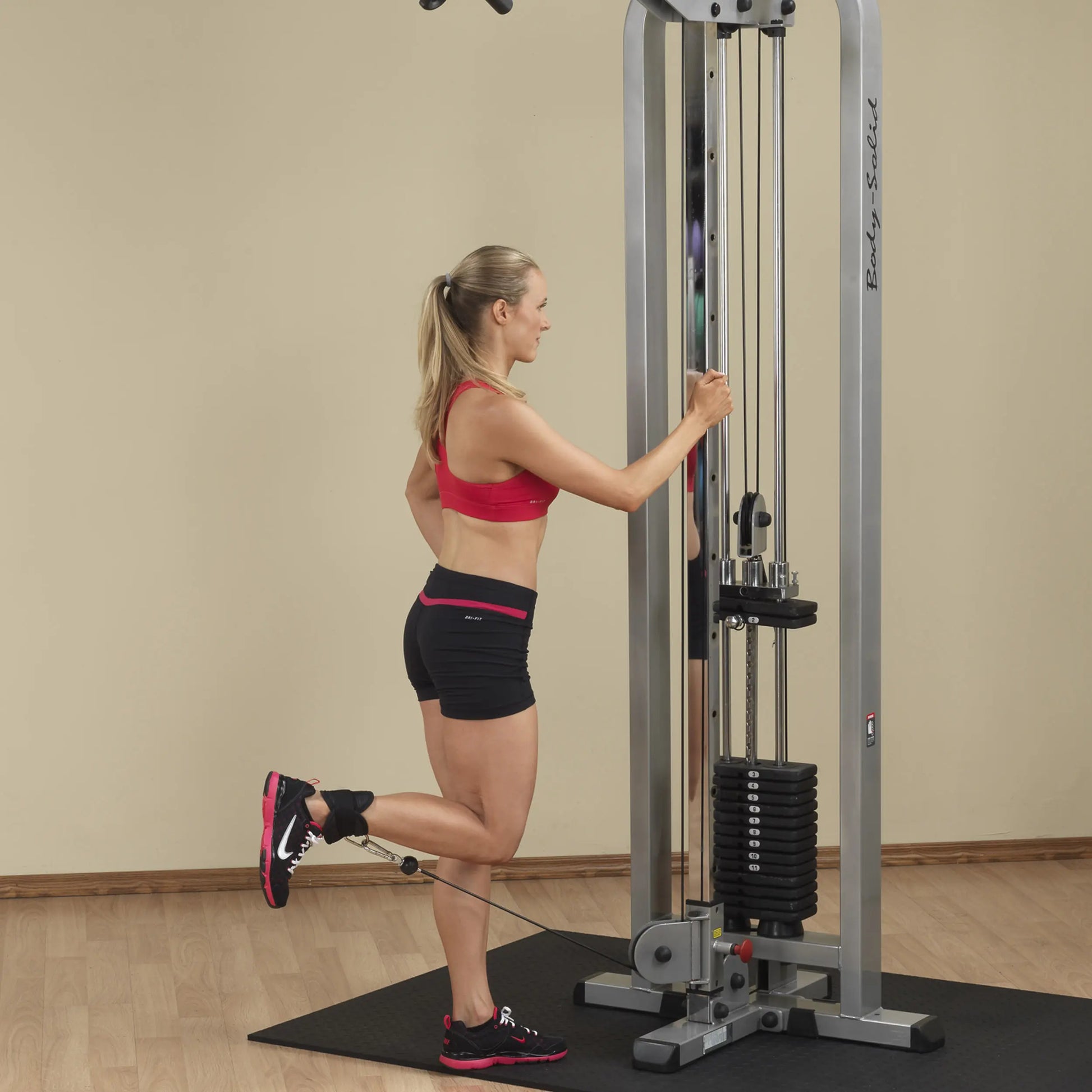 Woman using the Body-Solid Pro Clubline Cable Crossover SCC1200G for strength training, demonstrating a cable exercise with one leg elevated.