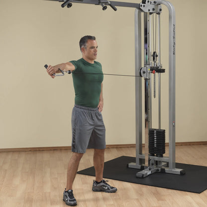 A man in a green shirt and gray shorts performing an exercise using the Body-Solid Pro Clubline Cable Crossover SCC1200G, demonstrating a cable crossover movement in a gym setting.