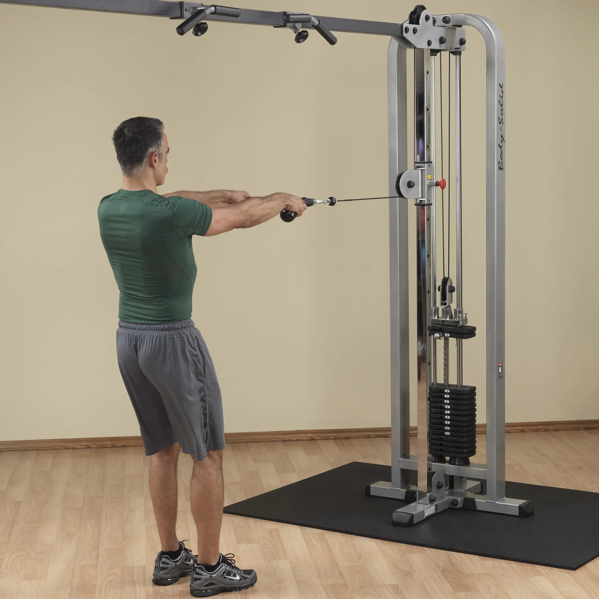 A man performing an exercise using the Body-Solid Pro Clubline Cable Crossover SCC1200G in a gym setting. He is pulling the cable handles towards him while standing on a rubber mat.