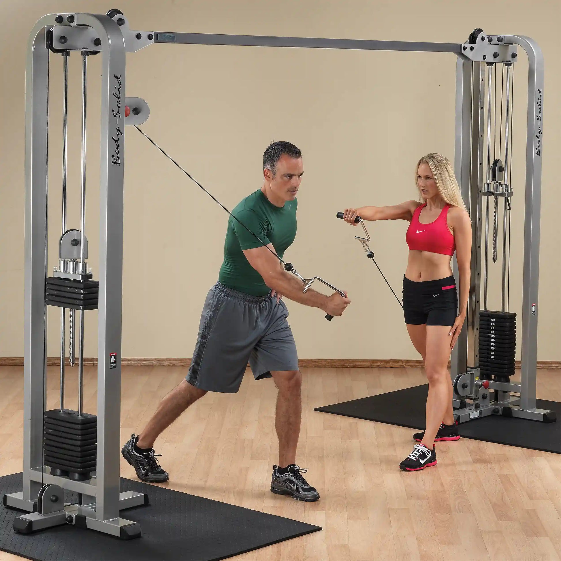 Two individuals using the Body-Solid Pro Clubline Cable Crossover SCC1200G for strength training exercises in a gym setting.