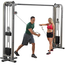 Two individuals using the Body-Solid Pro Clubline Cable Crossover SCC1200G for strength training, with one performing a cable crossover exercise while the other assists.