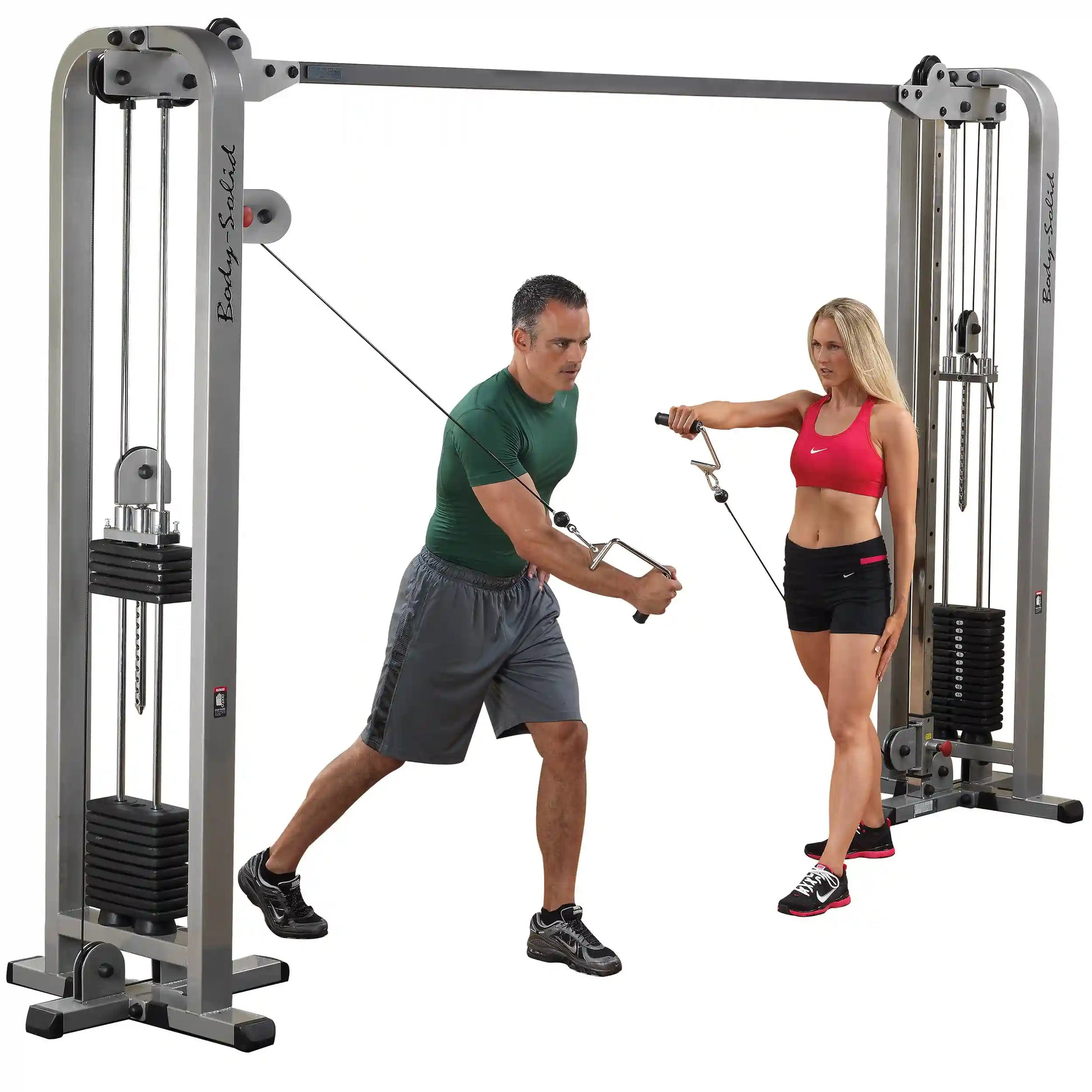 Two individuals using the Body-Solid Pro Clubline Cable Crossover SCC1200G for strength training, with one performing a cable crossover exercise while the other assists.
