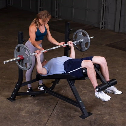 A woman assists a man lifting weights on the Body-Solid Pro Clubline Decline Olympic Bench SODB250 in a gym setting.