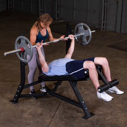 A person performing a bench press with the Body-Solid Pro Clubline Decline Olympic Bench SODB250, assisted by a trainer in a gym setting.