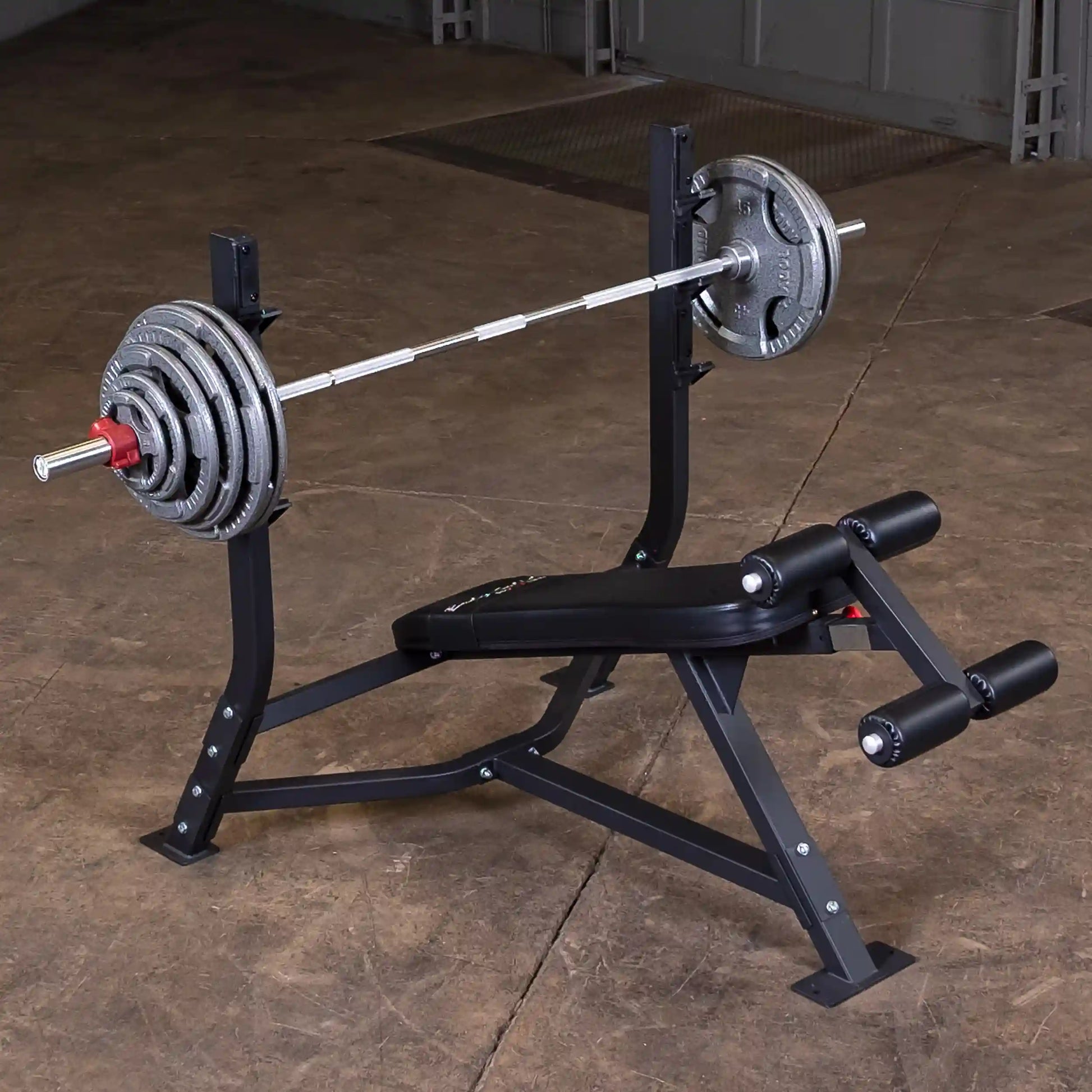Body-Solid Pro Clubline Decline Olympic Bench SODB250 with a barbell and weight plates, set on a gym floor.