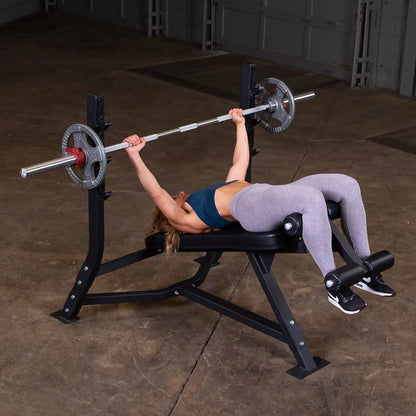 A woman performing a decline bench press on the Body-Solid Pro Clubline Decline Olympic Bench SODB250, with a barbell and weights above her, in a spacious gym setting.