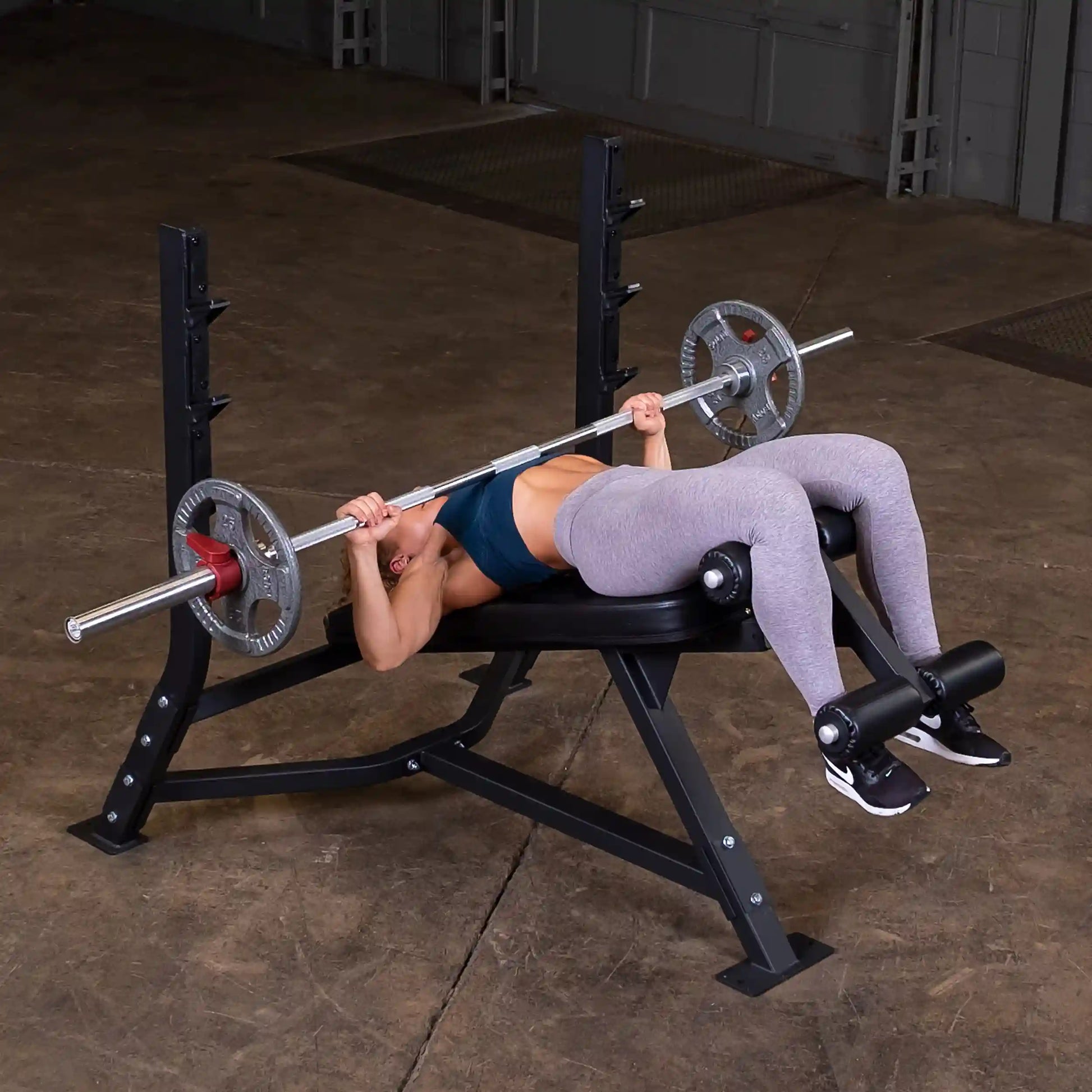 A person performing a decline bench press on the Body-Solid Pro Clubline Decline Olympic Bench SODB250, using a barbell with weights in a gym setting.