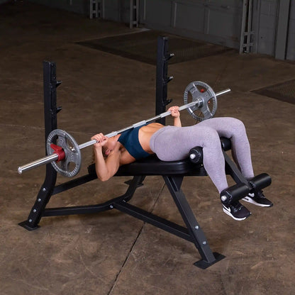 A person performing a decline bench press on the Body-Solid Pro Clubline Decline Olympic Bench SODB250, using a barbell with weights in a gym setting.