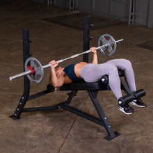A woman performing a decline bench press on the Body-Solid Pro Clubline Decline Olympic Bench SODB250, using a barbell with weights in a gym setting.
