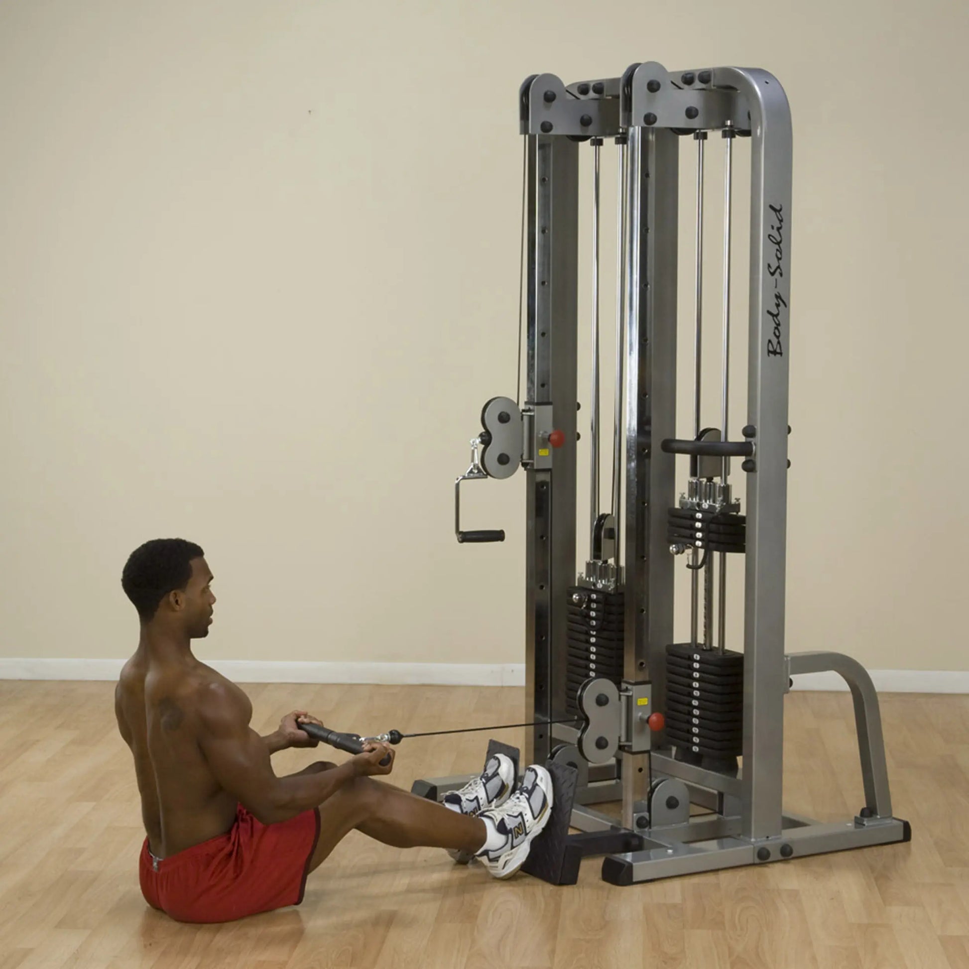 A man sitting on the floor using the Body-Solid Pro Clubline Dual Cable Column SDC2000G2 for a workout, with weights visible on the machine.